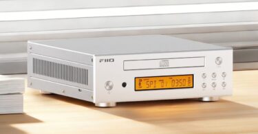 Lecteur CD de bureau FiiO DP11 en finition argent vu de trois quarts, avec tiroir CD frontal logo Compact Disc Digital Audio, écran LCD ambré, boutons de navigation ronds et flancs ajourés en aluminium