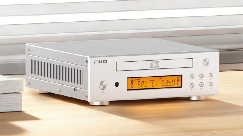 Lecteur CD de bureau FiiO DP11 en finition argent vu de trois quarts, avec tiroir CD frontal logo Compact Disc Digital Audio, écran LCD ambré, boutons de navigation ronds et flancs ajourés en aluminium