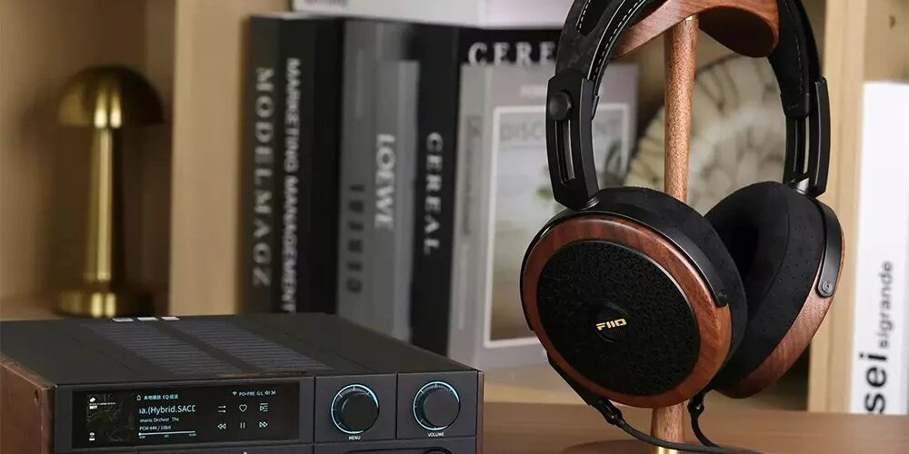 Casque planaire ouvert FiiO FT15 avec coques en noyer noir massif, grilles noires et logo doré, posé sur un support en bois à côté d'un DAC ampli casque de bureau FiiO à écran couleur, dans une bibliothèque