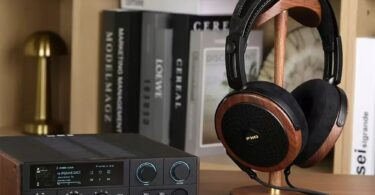Casque planaire ouvert FiiO FT15 avec coques en noyer noir massif, grilles noires et logo doré, posé sur un support en bois à côté d'un DAC ampli casque de bureau FiiO à écran couleur, dans une bibliothèque