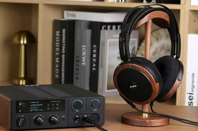 Casque planaire ouvert FiiO FT15 avec coques en noyer noir massif, grilles noires et logo doré, posé sur un support en bois à côté d'un DAC ampli casque de bureau FiiO à écran couleur, dans une bibliothèque