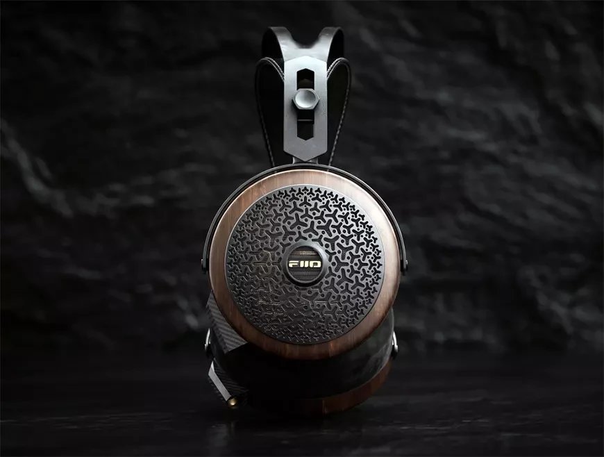 Vue de profil du casque planaire FiiO FT15 sur fond de pierre sombre, coque en noyer noir massif, grille ajourée laissant deviner le motif doré du transducteur planaire de 101 mm, étrier en fibre de carbone et connecteur 3,5 mm