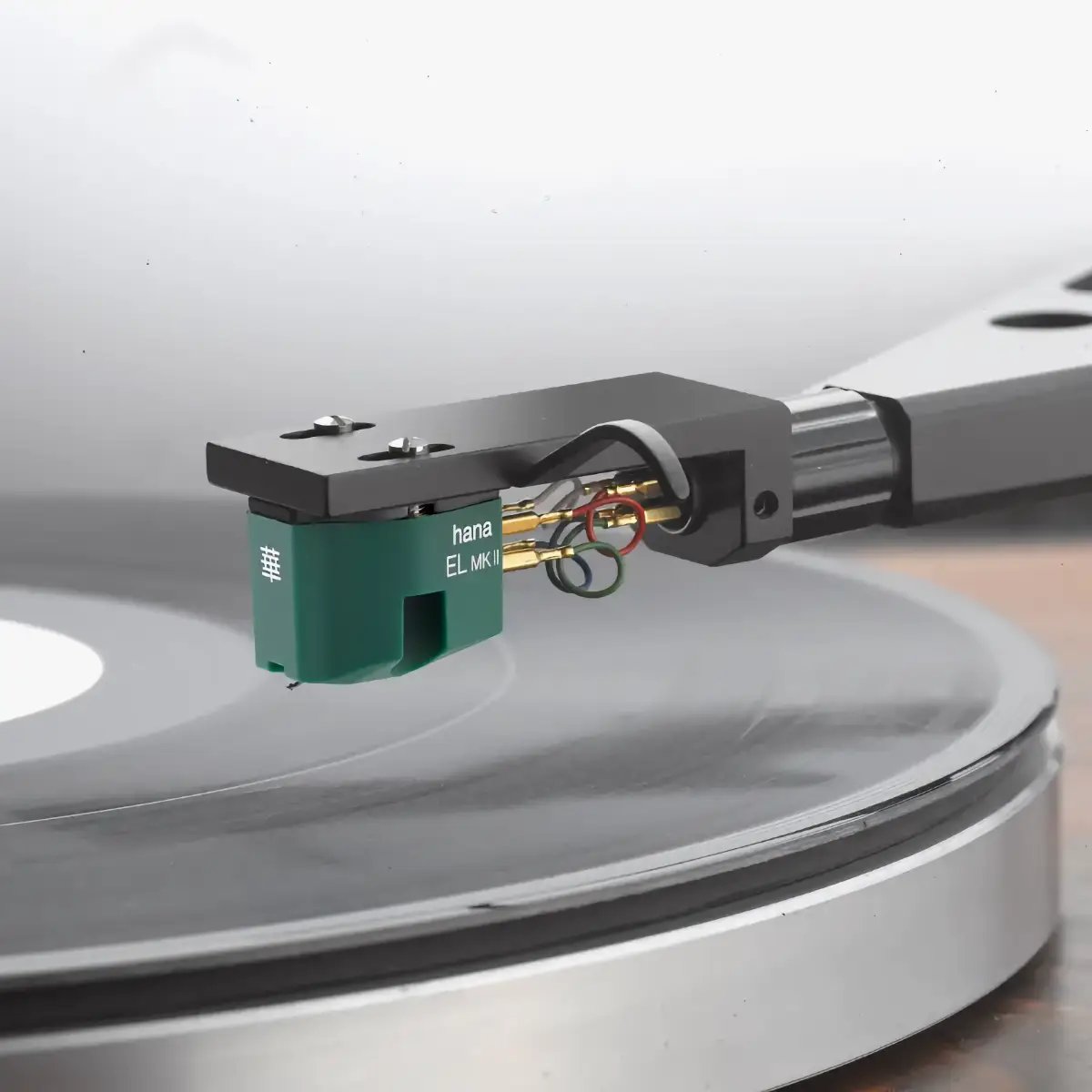 Cellule phono Hana EL Mk II à bobine mobile bas niveau, corps vert mousse, fixée par deux vis sur une coquille noire, broches plaquées or et fils de liaison colorés, diamant posé dans le sillon d'un disque vinyle