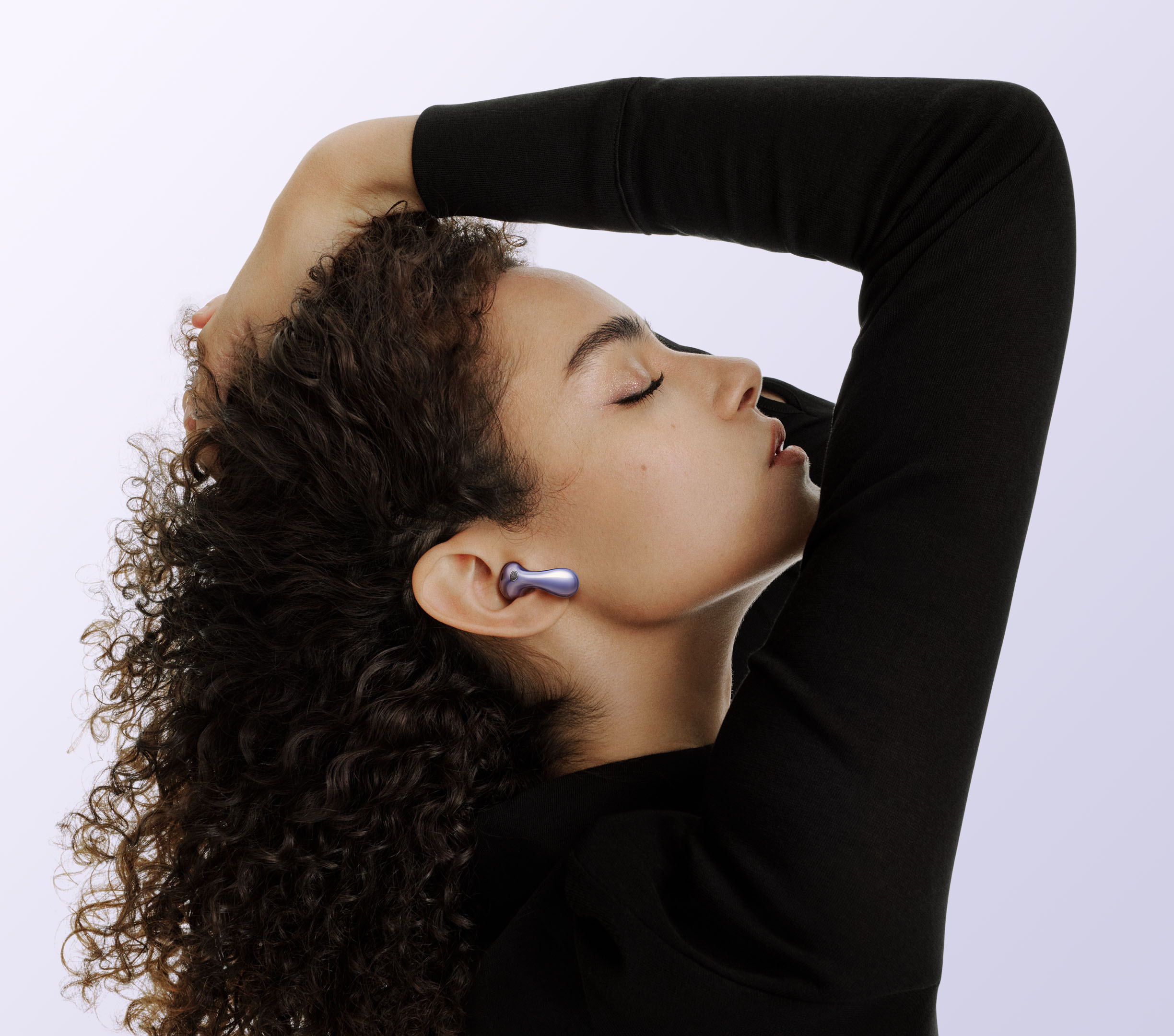Femme de profil portant un écouteur Huawei FreeBuds 6 violet à finition miroir, logé dans la conque sans embout silicone dans le conduit auditif, corps en goutte d'eau et anse galbée épousant le pavillon, fond lilas clair