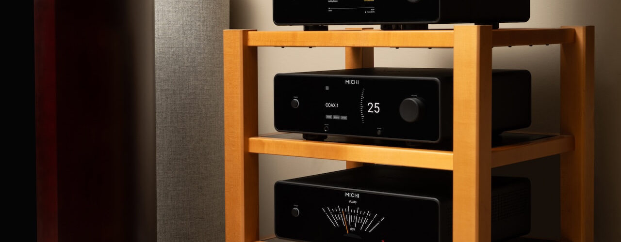 Trois appareils Michi Prestige empilés, lecteur CD Q430, préampli P430 et ampli S430, avec façades noires, écrans TFT couleur et vumètre, près d'une enceinte colonne