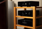 Trois appareils Michi Prestige empilés, lecteur CD Q430, préampli P430 et ampli S430, avec façades noires, écrans TFT couleur et vumètre, près d'une enceinte colonne