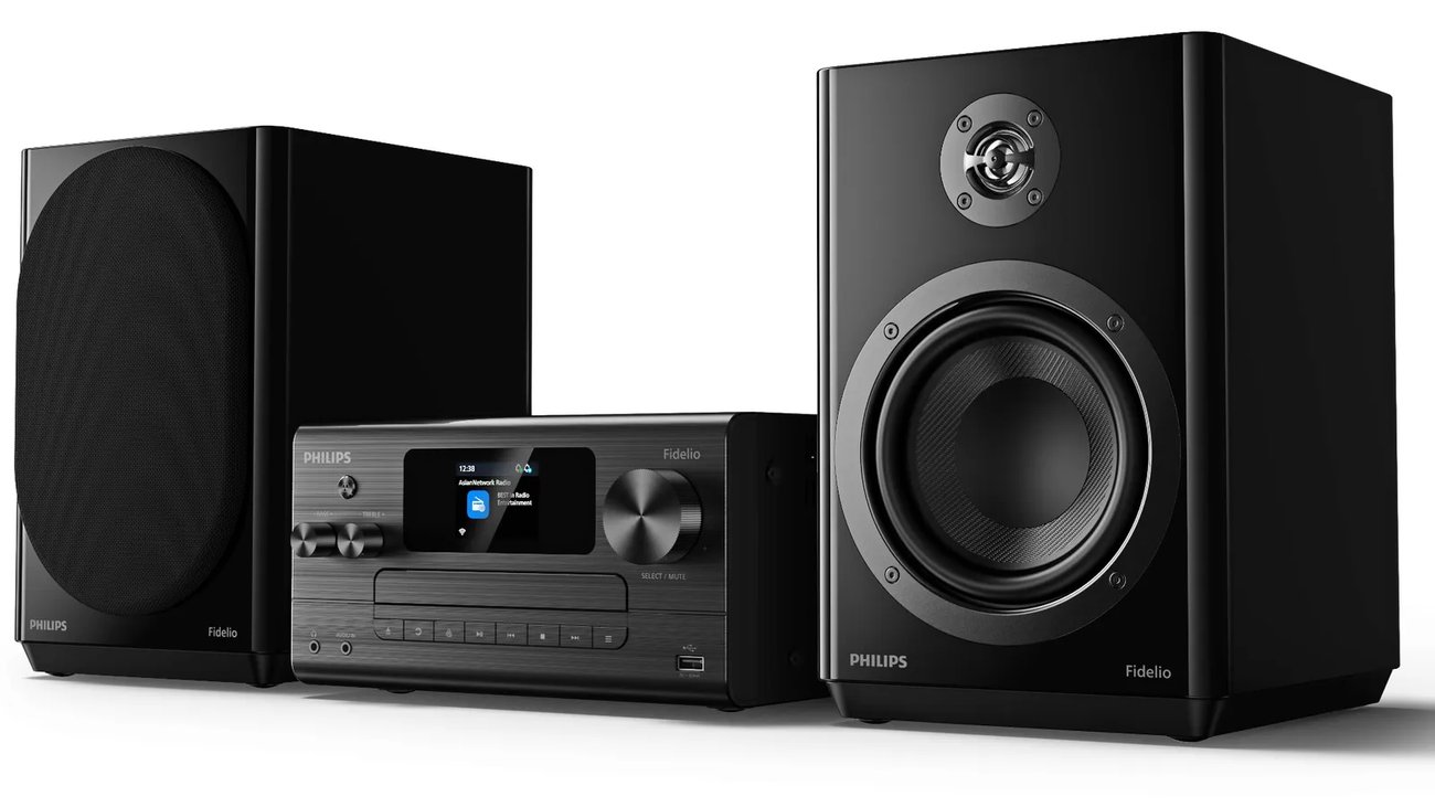 Philips Fidelio FA7 sur fond blanc : unité centrale noire avec écran couleur, tiroir CD, molettes basses et aigus, bouton Select/Mute, prises casque, Audio In et USB en façade, enceinte droite sans grille montrant tweeter titane et woofer
