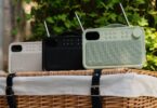 Trois radios portables Pure Bloom DAB+ et Bluetooth en coloris Sable, Noir et Sauge posées sur un panier de pique-nique en osier, avec antennes télescopiques, écran couleur, touches de présélection et façade en tissu