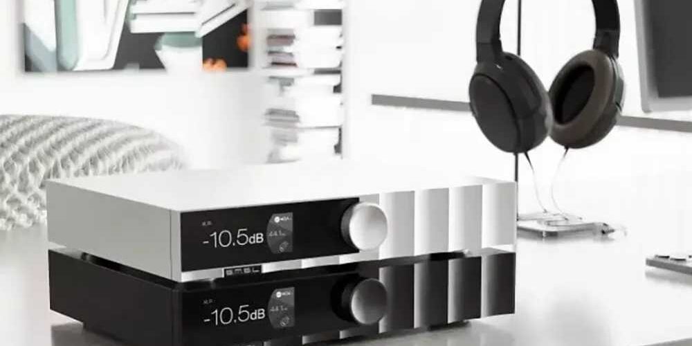 Deux SMSL D400 MK2 empilés sur un meuble de salon, finition argent en haut et noire en bas, façade en aluminium usiné CNC avec afficheur IPS sous verre laminé indiquant -10,5 dB et 44,1 kHz, gros bouton rotatif de volume, casque circum-aural sur son support en arrière-plan