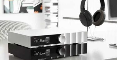 Deux SMSL D400 MK2 empilés sur un meuble de salon, finition argent en haut et noire en bas, façade en aluminium usiné CNC avec afficheur IPS sous verre laminé indiquant -10,5 dB et 44,1 kHz, gros bouton rotatif de volume, casque circum-aural sur son support en arrière-plan