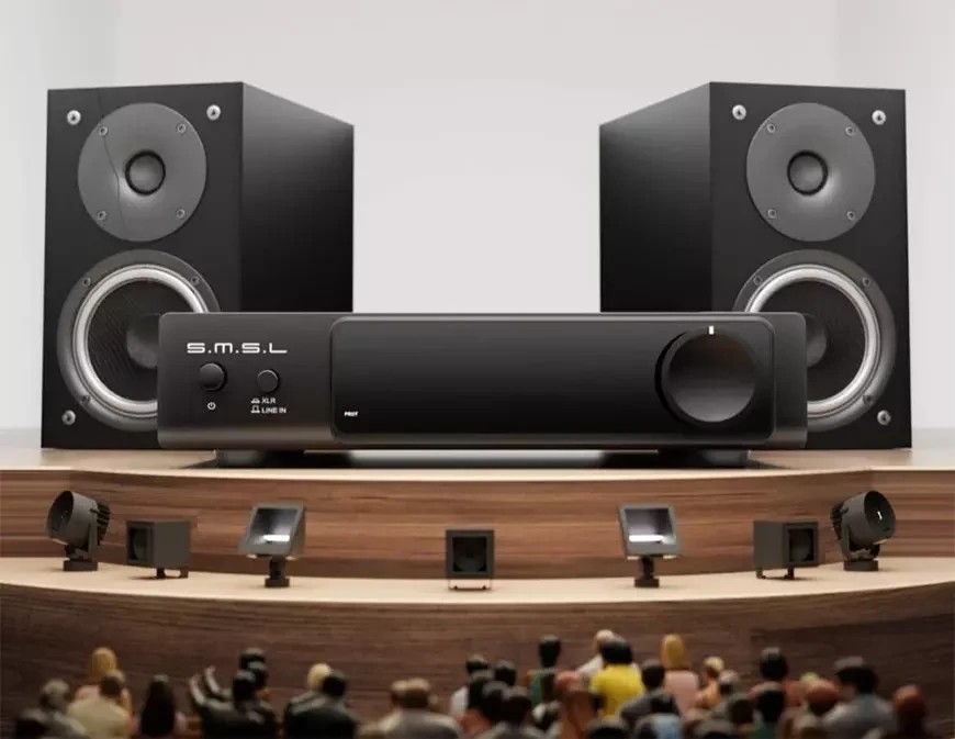 Amplificateur de puissance SMSL RAW-MHA1 vu de face devant deux enceintes de bibliothèque noires à deux voies, avec sélecteur d'entrée XLR et LINE IN, témoin PROT et large potentiomètre de niveau, posé sur une scène de concert stylisée