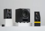 Caisson de basses actif ADAM Audio Sub8 PRO noir avec grille métallique et évent frontal moucheté, posé entre deux moniteurs de studio ADAM série A sur fond gris clair