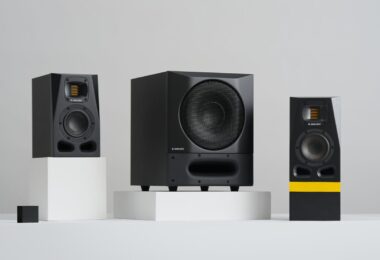 Caisson de basses actif ADAM Audio Sub8 PRO noir avec grille métallique et évent frontal moucheté, posé entre deux moniteurs de studio ADAM série A sur fond gris clair