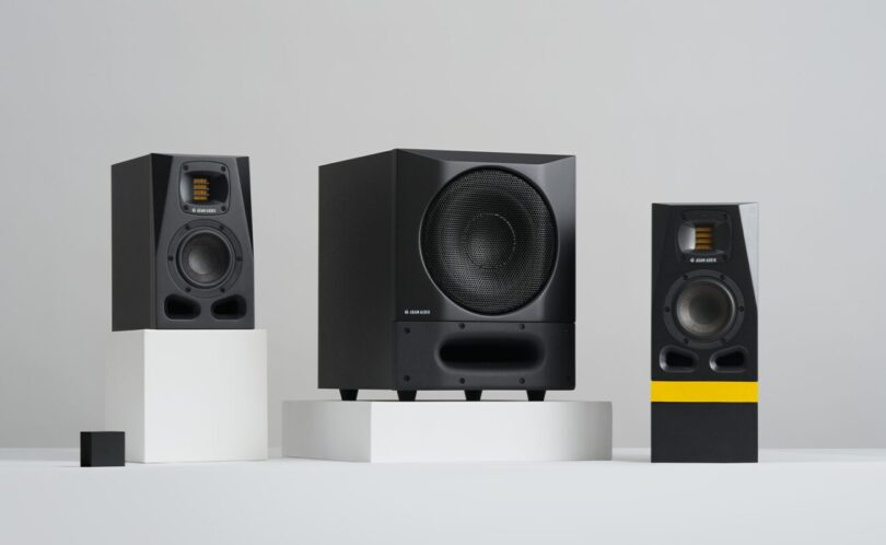 Caisson de basses actif ADAM Audio Sub8 PRO noir avec grille métallique et évent frontal moucheté, posé entre deux moniteurs de studio ADAM série A sur fond gris clair