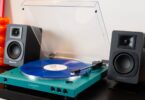 Platine vinyle Audio-Technica AT-LP60XBT en finition bleu canard avec couvercle ouvert et vinyle bleu sur le plateau, entourée de deux enceintes actives noires sur un meuble