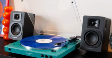Platine vinyle Audio-Technica AT-LP60XBT en finition bleu canard avec couvercle ouvert et vinyle bleu sur le plateau, entourée de deux enceintes actives noires sur un meuble