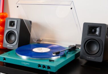 Platine vinyle Audio-Technica AT-LP60XBT en finition bleu canard avec couvercle ouvert et vinyle bleu sur le plateau, entourée de deux enceintes actives noires sur un meuble