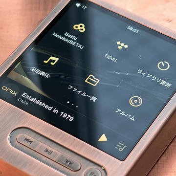 Gros plan sur un baladeur audiophile Onix à châssis cuivré : écran tactile avec les icônes TIDAL, bibliothèque musicale et albums, mention « Established in 1979 » et trois touches de lecture physiques en façade