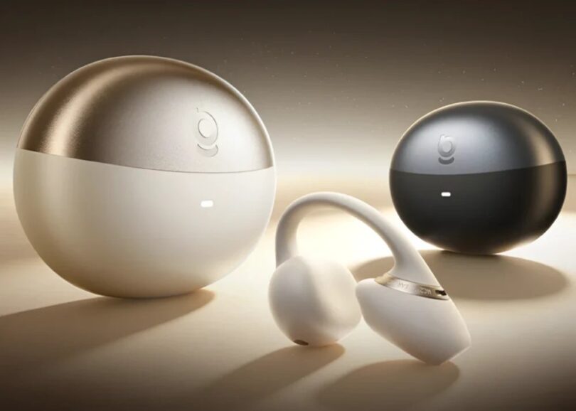 Écouteur open-ear à clip Baseus MC2 NC beige avec arceau en C et bague dorée, posé devant ses boîtiers de charge sphériques beige champagne et noir avec indicateur lumineux