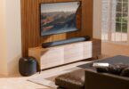 Barre de son Bluesound Pulse Cinema sous un téléviseur et caisson Pulse Sub posé au sol dans un salon, deux appareils BluOS qui reçoivent Apple Music en natif
