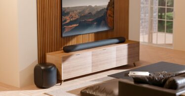 Barre de son Bluesound Pulse Cinema sous un téléviseur et caisson Pulse Sub posé au sol dans un salon, deux appareils BluOS qui reçoivent Apple Music en natif