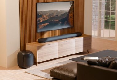 Barre de son Bluesound Pulse Cinema sous un téléviseur et caisson Pulse Sub posé au sol dans un salon, deux appareils BluOS qui reçoivent Apple Music en natif