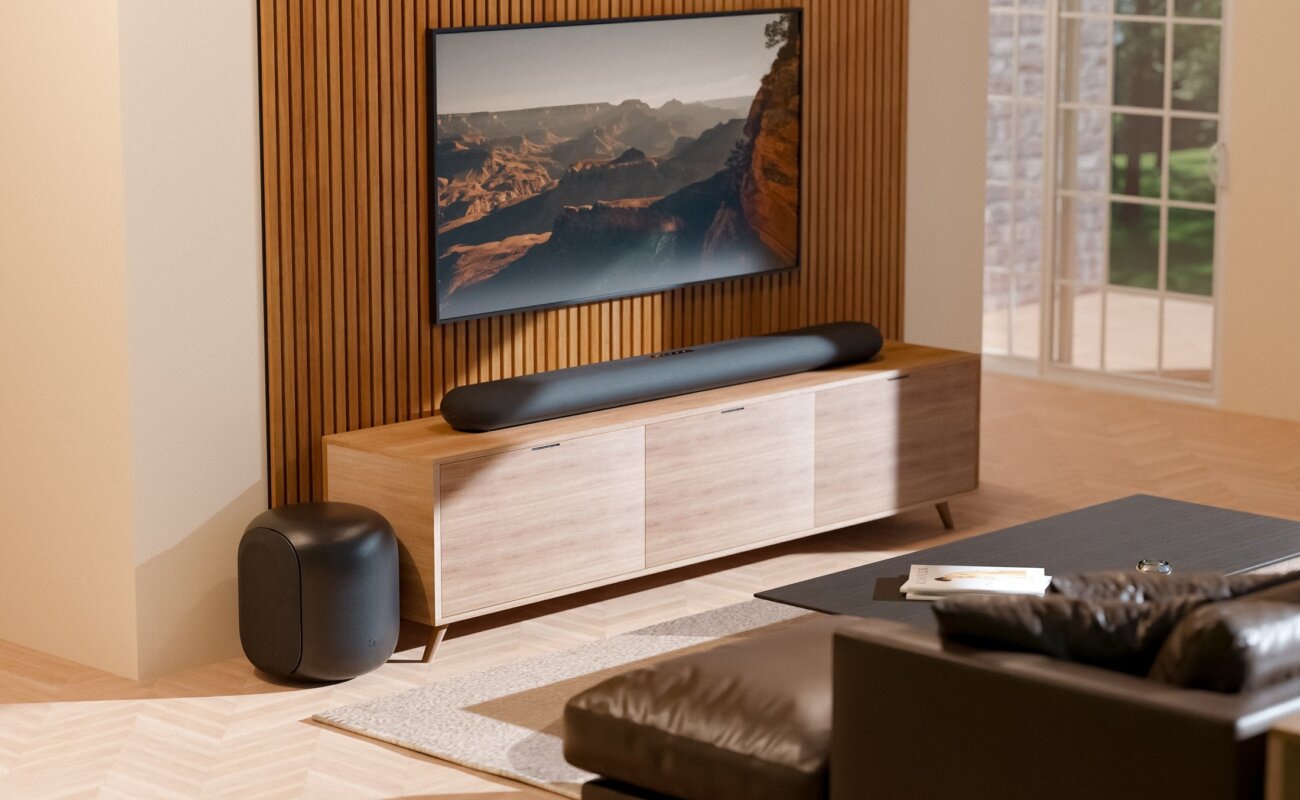 Barre de son Bluesound Pulse Cinema sous un téléviseur et caisson Pulse Sub posé au sol dans un salon, deux appareils BluOS qui reçoivent Apple Music en natif