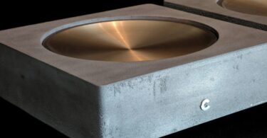 DAC Cinnamon Galle Model II : châssis en aluminium coulé au sable, dessus en bronze ciré à la main en forme de coupelle, logo Cinnamon en façade, second châssis en arrière-plan