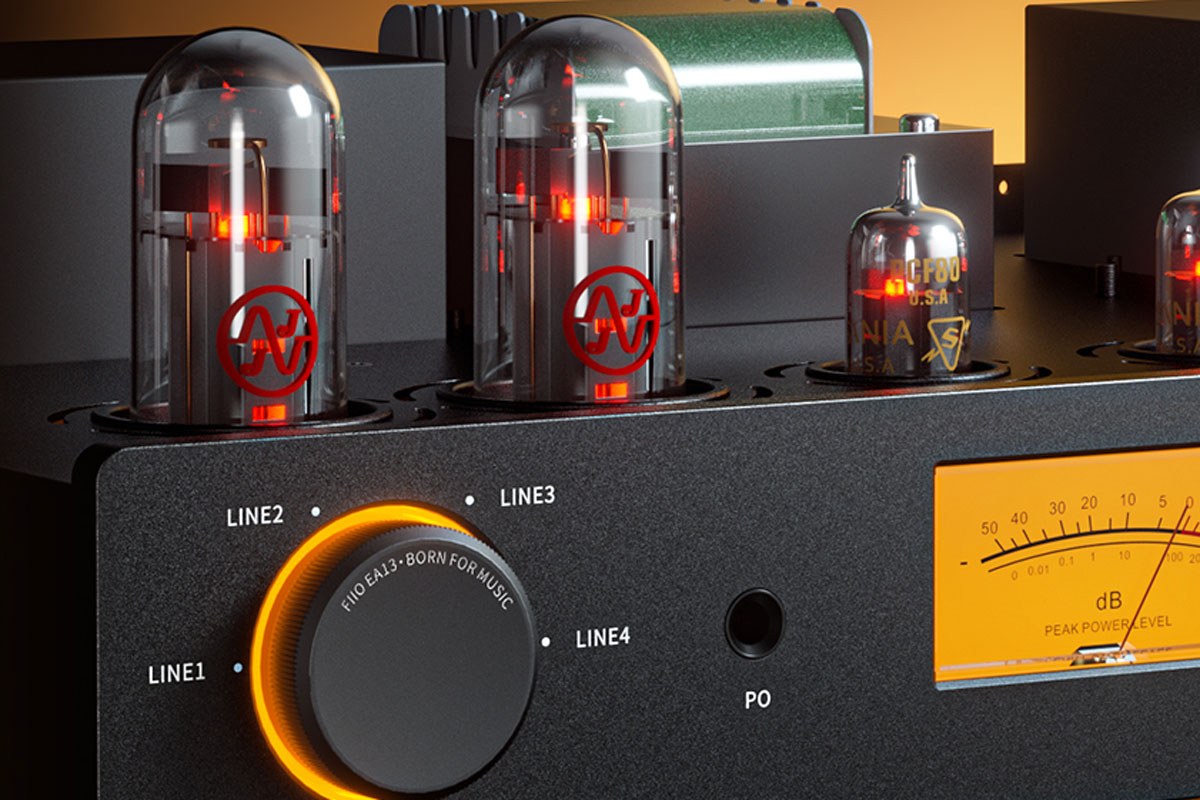 Gros plan sur le FiiO EA13 noir : deux lampes de puissance JJ Electronic EL34 allumées, un tube Sylvania NOS PCF80, sélecteur d'entrées LINE1 à LINE4 à anneau lumineux orange, prise casque PO et VU-mètre ambré