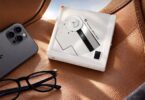 Lecteur CD portable Fosi Audio DISC Nano en finition blanche posé sur un siège en cuir fauve, disque à moitié apparent, rangée de boutons en façade, à côté d'un smartphone et de lunettes
