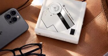 Lecteur CD portable Fosi Audio DISC Nano en finition blanche posé sur un siège en cuir fauve, disque à moitié apparent, rangée de boutons en façade, à côté d'un smartphone et de lunettes
