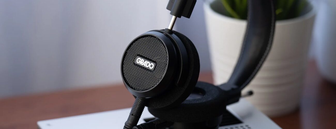 Casque ouvert Grado Signature S150 noir posé sur un appareil hi-fi argenté, grille de la coque avec logo Grado, arceau en cuir et câble détachable
