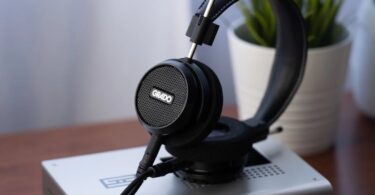 Casque ouvert Grado Signature S150 noir posé sur un appareil hi-fi argenté, grille de la coque avec logo Grado, arceau en cuir et câble détachable
