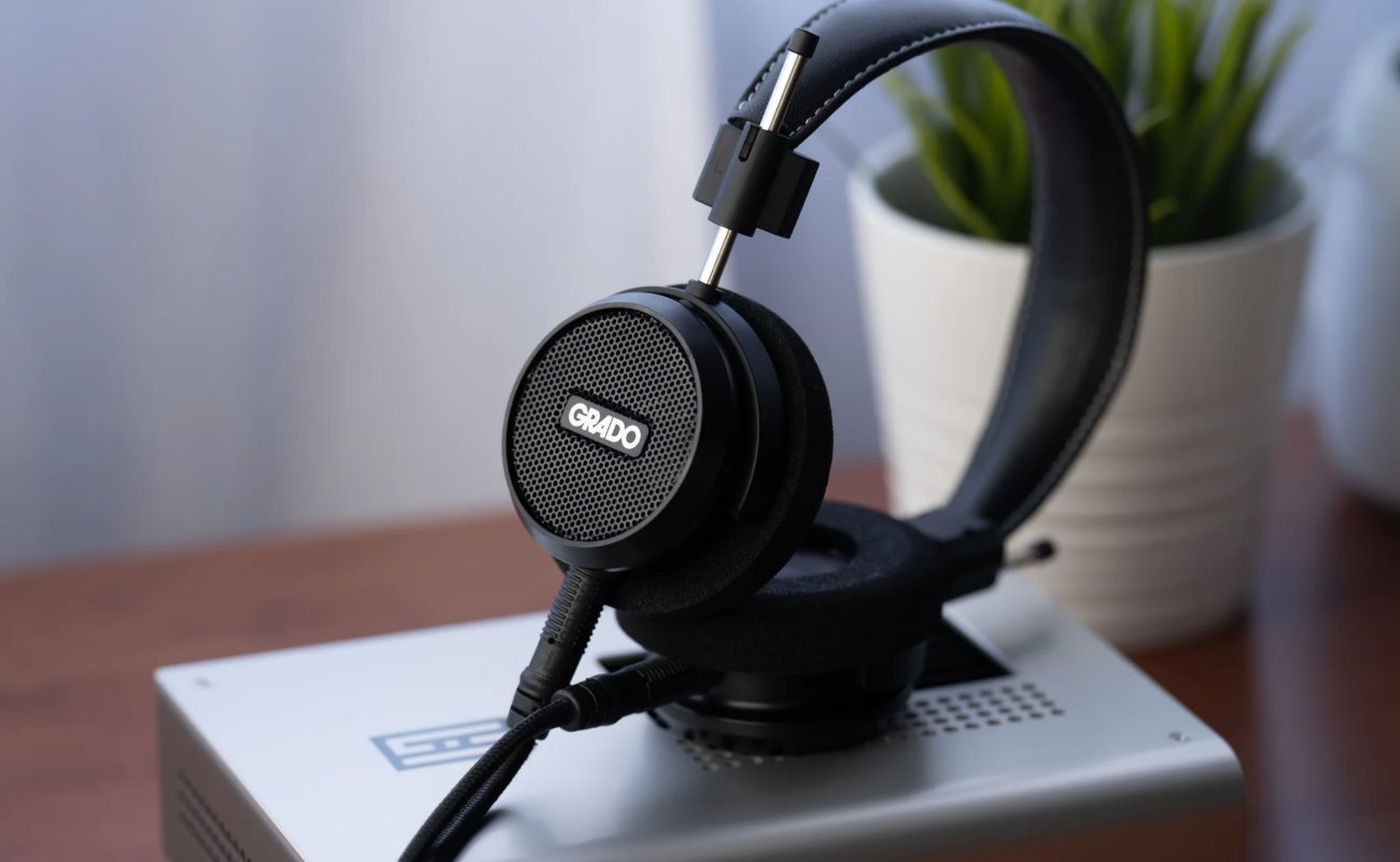 Casque ouvert Grado Signature S150 noir posé sur un appareil hi-fi argenté, grille de la coque avec logo Grado, arceau en cuir et câble détachable