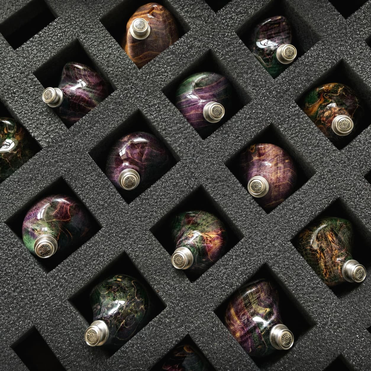 Série de coques Grand Oriveti Eminency en bois stabilisé et résine aux teintes violettes, vertes et terre, rangées dans une mousse alvéolée noire