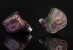 Paire d'intra-auriculaires Grand Oriveti Eminency à coque en bois stabilisé et résine aux tons violets et verts, façade à incrustation dorée, sur fond noir réfléchissant