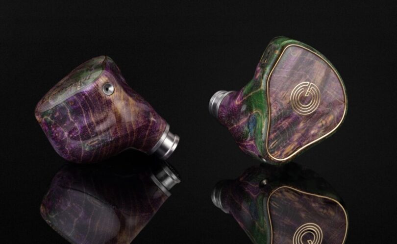 Paire d'intra-auriculaires Grand Oriveti Eminency à coque en bois stabilisé et résine aux tons violets et verts, façade à incrustation dorée, sur fond noir réfléchissant