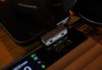 Émetteur Bluetooth iFi UP Play Max branché en USB-C, avec ses boutons d'appairage et de codec, à côté d'un casque, compatible aptX Lossless et LDAC