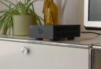 Ampli de puissance stéréo IOTAVX B:ound noir posé sur un meuble blanc, boîtier compact de 16,4 cm à ouïes d'aération latérales et bouton de mise en marche lumineux