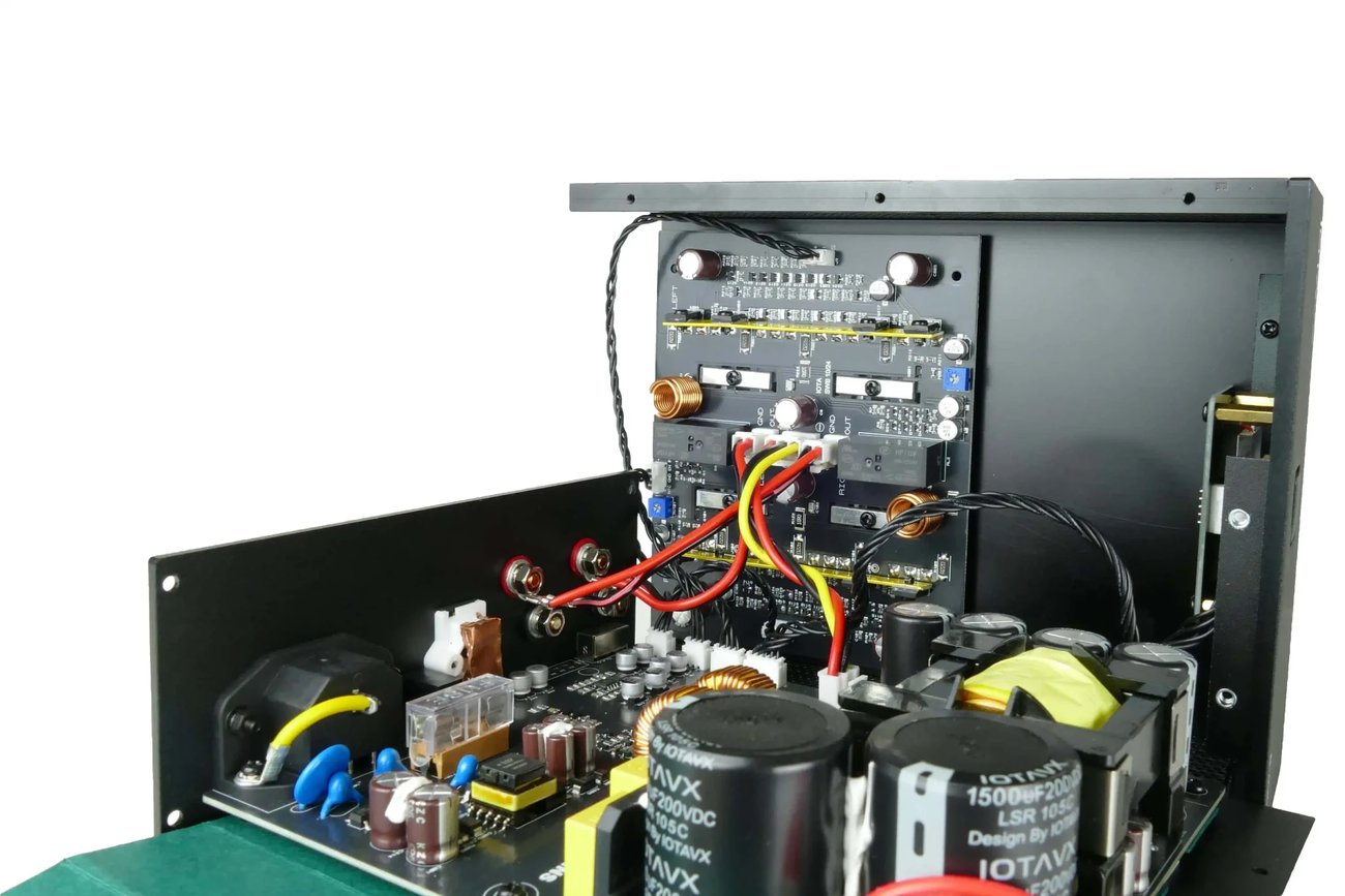 Intérieur de l'IOTAVX B:ound : alimentation à découpage avec gros condensateurs de filtrage siglés IOTAVX au premier plan, carte d'amplification classe B verticale et entrées RCA sur le panneau arrière