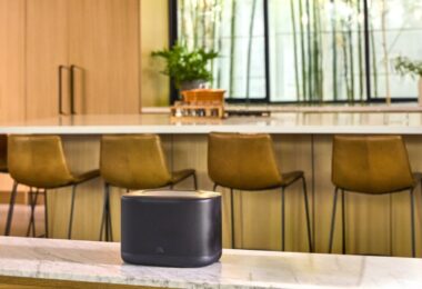 Enceinte multiroom Wi-Fi JBL Cove X1 noire posée sur un plan de travail en marbre dans une cuisine lumineuse avec tabourets de bar