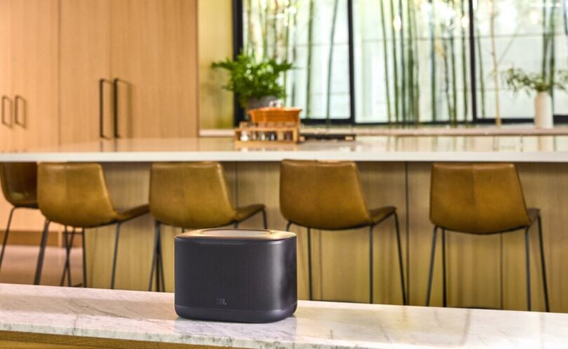 Enceinte multiroom Wi-Fi JBL Cove X1 noire posée sur un plan de travail en marbre dans une cuisine lumineuse avec tabourets de bar
