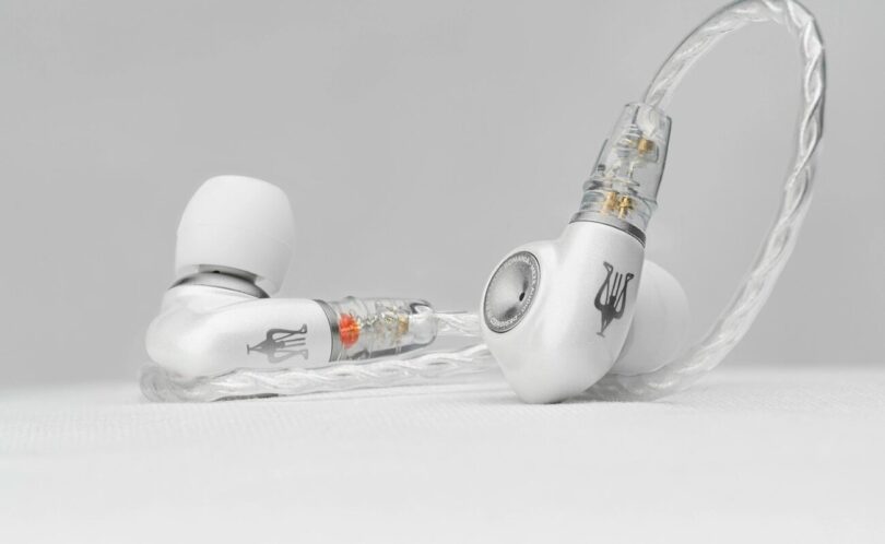 Intra-auriculaire Meze Audio ALBA S posé sur une surface claire, coque en alliage de zinc et aluminium anodisé blanc nacré, embout argenté et câble tressé argenté à connecteurs 2 broches