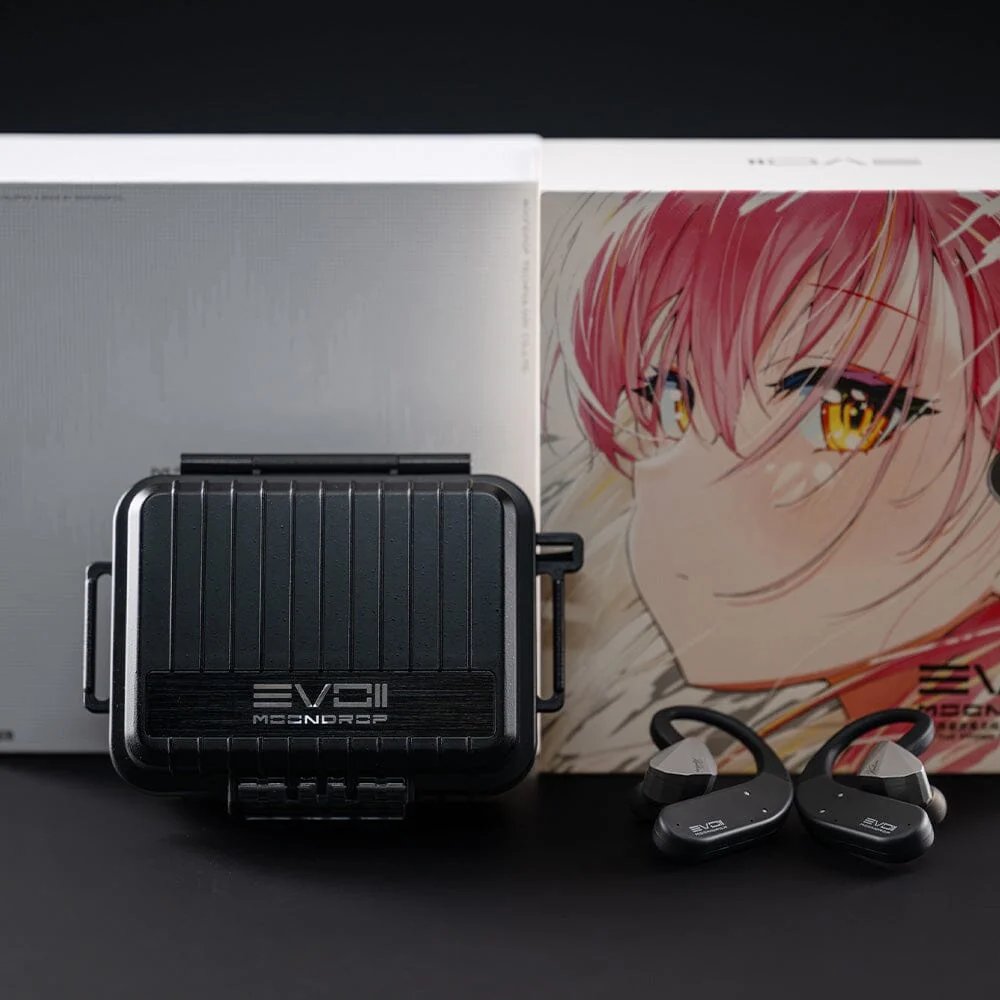 Coffret du Moondrop EVO 2 avec sa boîte blanche et sa boîte illustrée façon manga, devant lesquelles sont posés l'étui de charge rigide noir fermé marqué EVO II et les deux crochets Bluetooth montés sur des écouteurs argentés