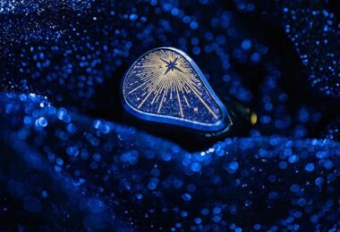 Écouteur intra-auriculaire Moondrop Starfield 3 posé sur un tissu bleu scintillant, plaque de façade bleu nuit pailletée avec étoile et rayons dorés