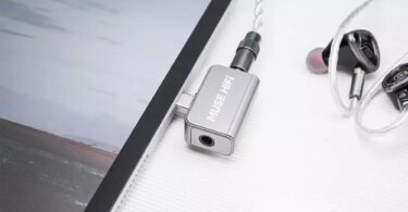 Dongle DAC Muse HiFi U3 en aluminium argent branché sur le port USB-C d'une tablette, avec des écouteurs intra-auriculaires reliés à sa prise jack 3,5 mm
