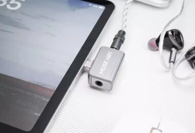 Dongle DAC Muse HiFi U3 en aluminium argent branché sur le port USB-C d'une tablette, avec des écouteurs intra-auriculaires reliés à sa prise jack 3,5 mm