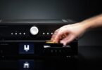 Lecteur CD Musical Fidelity B1xcd noir posé sous l amplificateur intégré B1xi, une main insérant un disque dans le tiroir