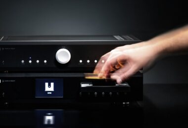 Lecteur CD Musical Fidelity B1xcd noir posé sous l amplificateur intégré B1xi, une main insérant un disque dans le tiroir