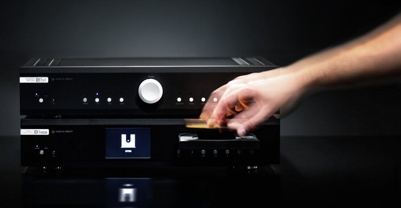 Lecteur CD Musical Fidelity B1xcd noir posé sous l amplificateur intégré B1xi, une main insérant un disque dans le tiroir